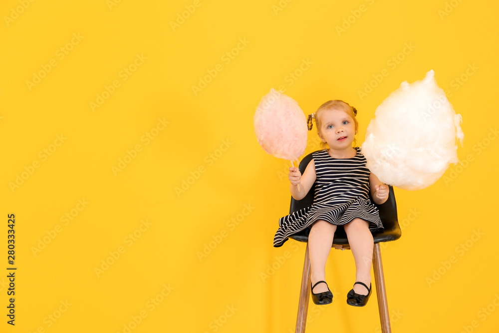 Cute little girl with cotton candy sitting on chair against color background