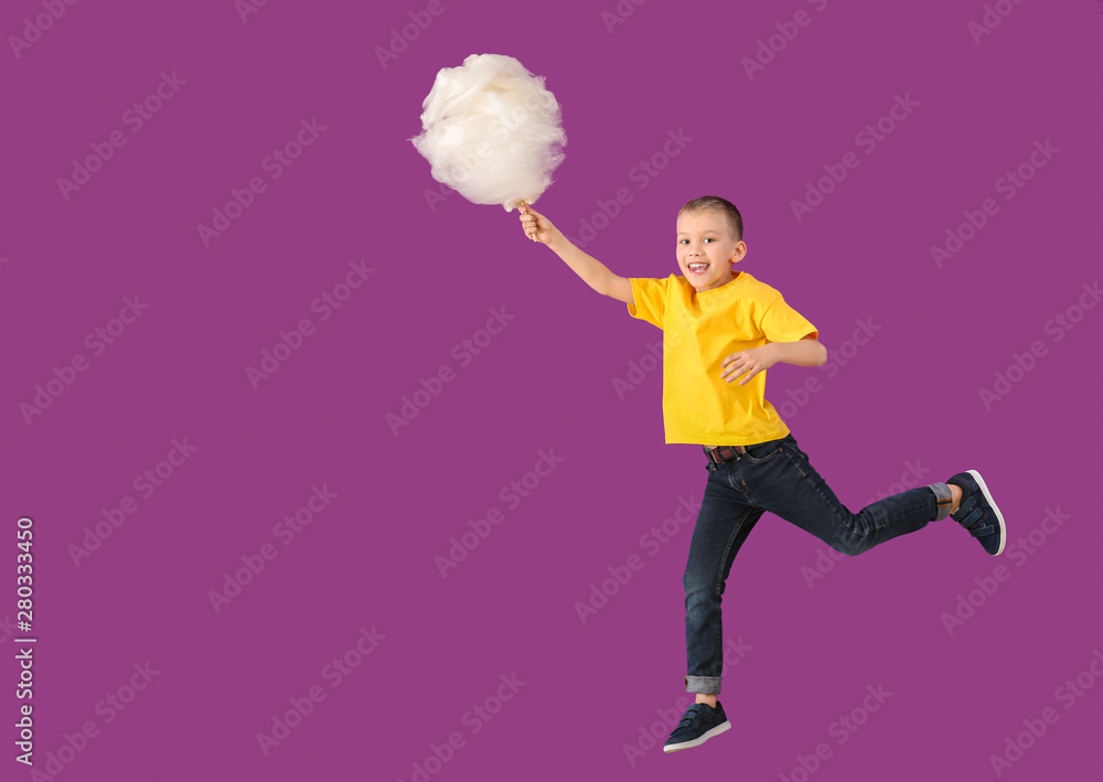 Jumping little boy with cotton candy on color background