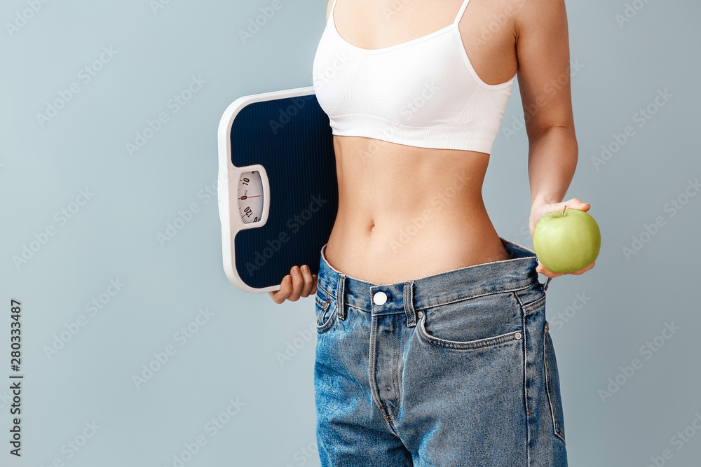 Young woman with scales and apple on color background. Weight loss concept