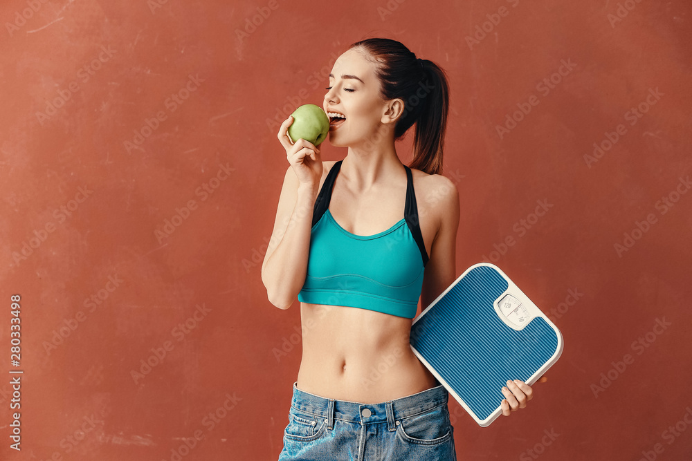 Young woman with scales and apple on color background. Weight loss concept