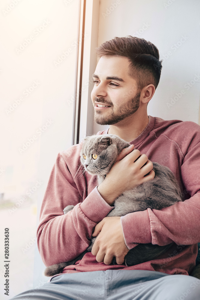 Young man with cute funny cat near window