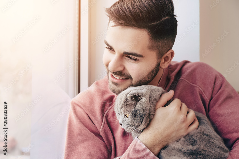 Young man with cute funny cat near window