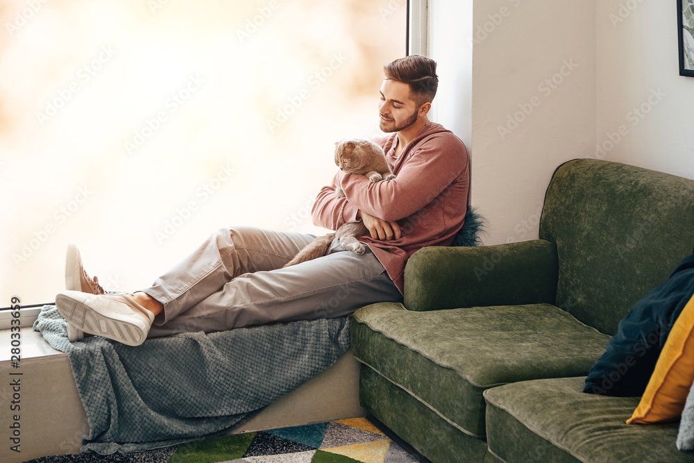 Young man with cute funny cat near window