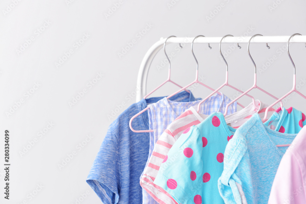 Stylish kid clothes hanging on rack against light background