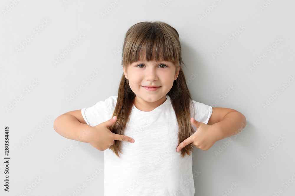 Little girl pointing at her t-shirt on light background