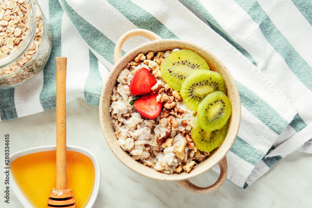 Pot with tasty sweet oatmeal, fruits and honey on light table