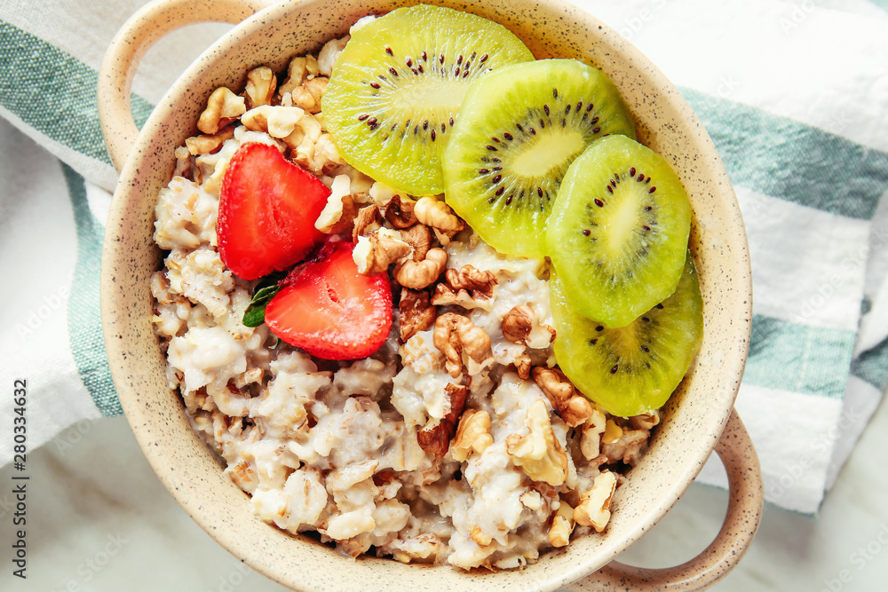 Pot with tasty sweet oatmeal, fruits and nut on table