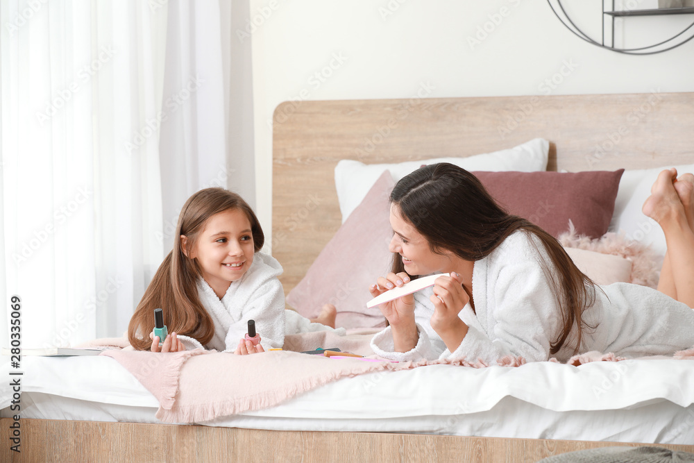 Mother and her little daughter in bathrobes doing nails in bedroom