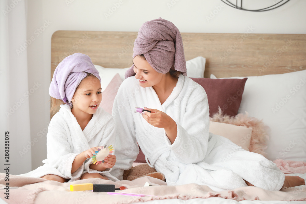 Mother and her little daughter in bathrobes manicuring nails in bedroom