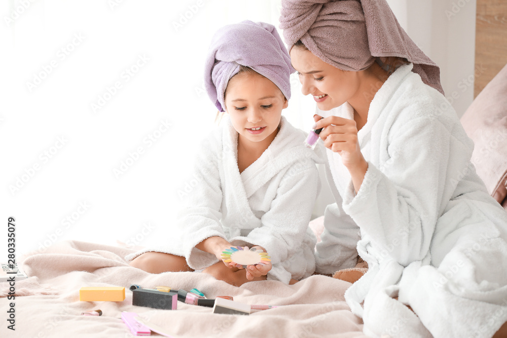 Mother and her little daughter in bathrobes manicuring nails in bedroom