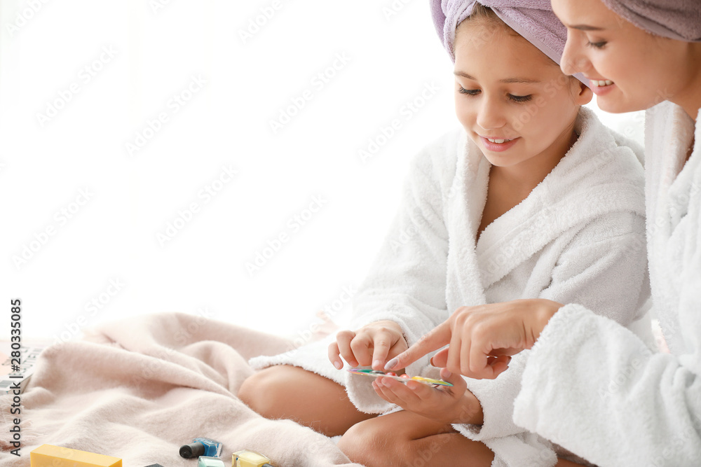 Mother and her little daughter in bathrobes manicuring nails in bedroom