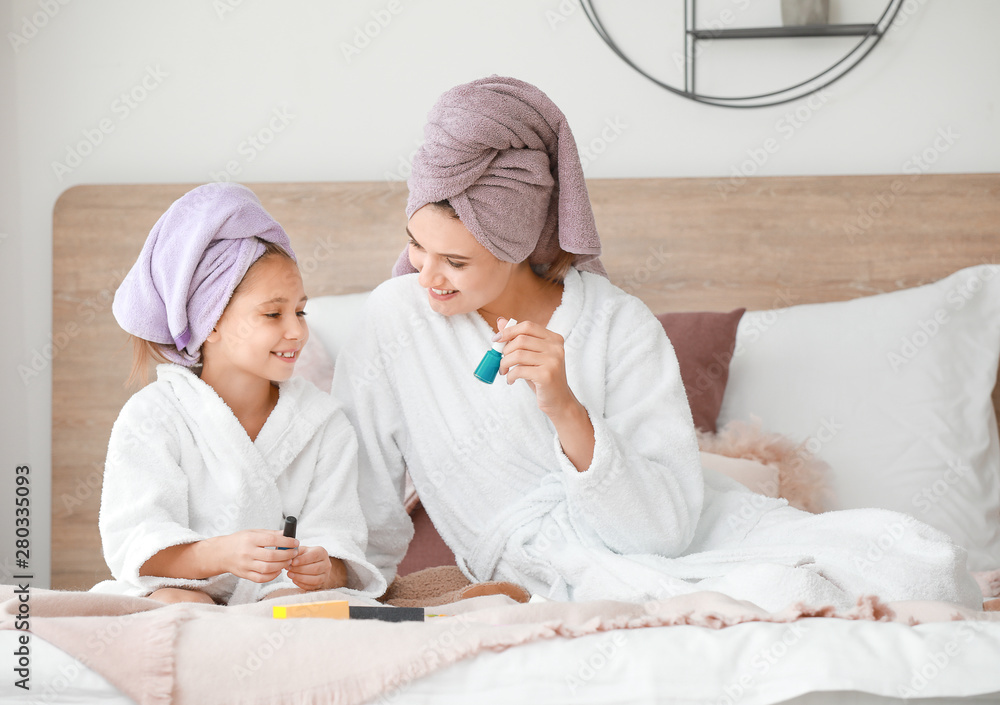 Mother and her little daughter in bathrobes manicuring nails in bedroom