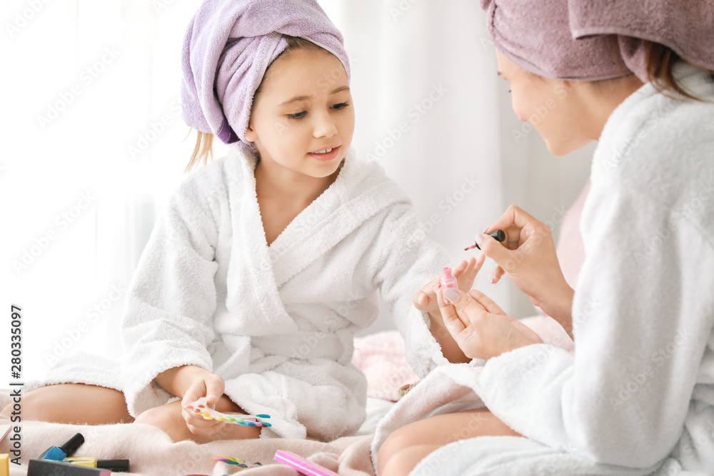 Mother and her little daughter in bathrobes manicuring nails in bedroom