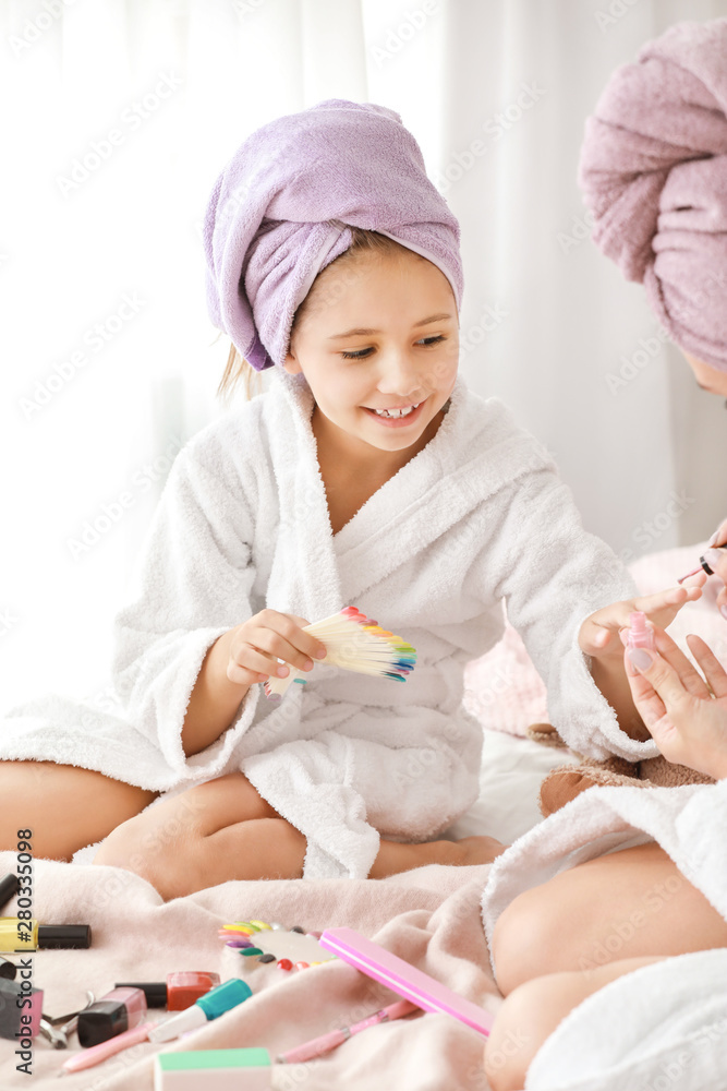 Mother and her little daughter in bathrobes manicuring nails in bedroom