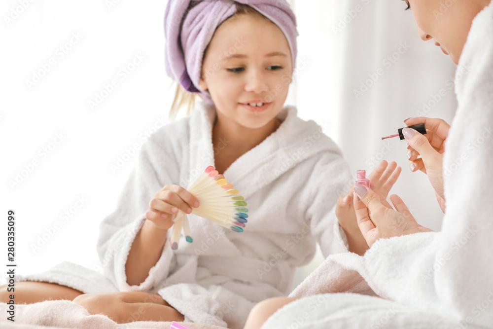 Mother and her little daughter in bathrobes manicuring nails in bedroom