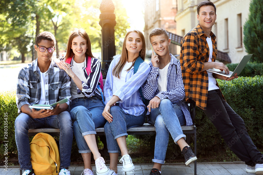 Young students sitting on bench outdoors