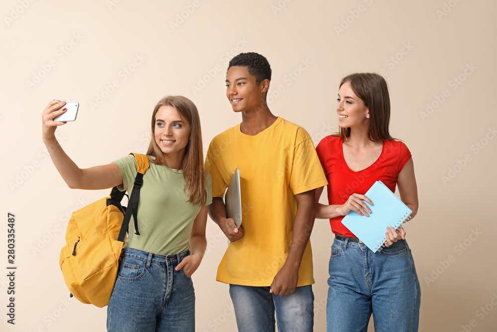 Portrait of young students taking selfie on light background