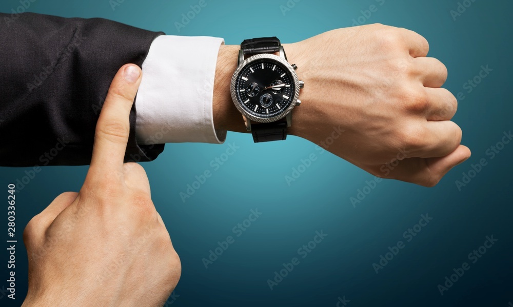 Businessman pointing at hand watch on grey wall background, close-up