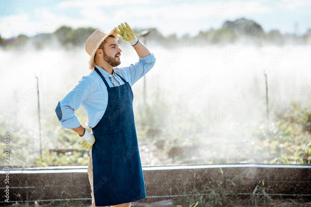 Portrait of a handsome farmer in blue workwear and straw hat standing on the farmland with automatic