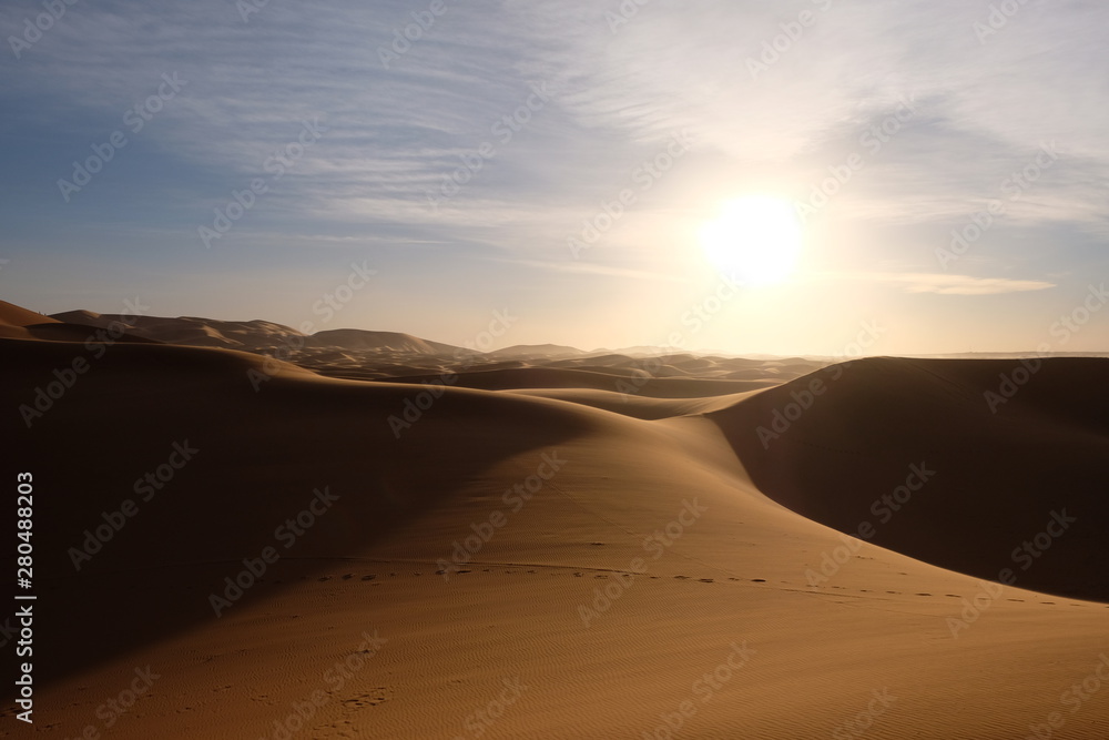 wild brown Sahara desert sand dunes at sunset. Strong shining sun with white cloud. footsteps and sh