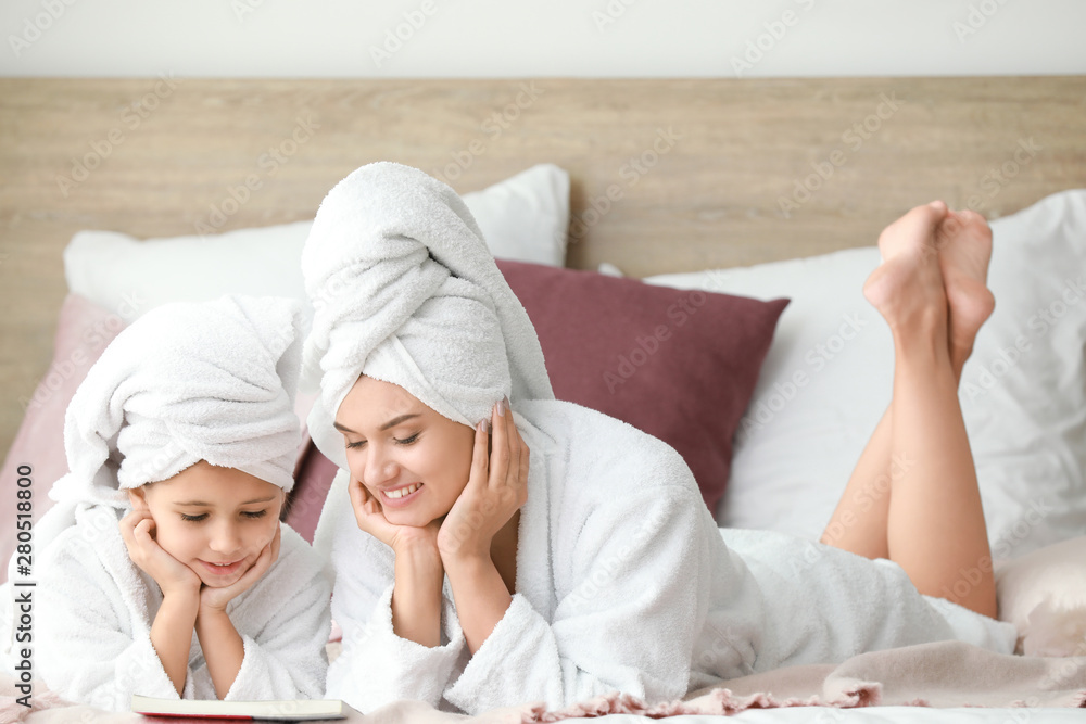 Mother and her little daughter in bathrobes relaxing in bedroom