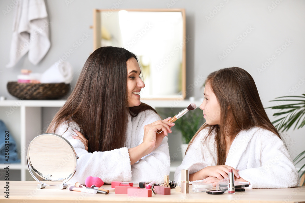 Mother and her little daughter in bathrobes applying makeup at home