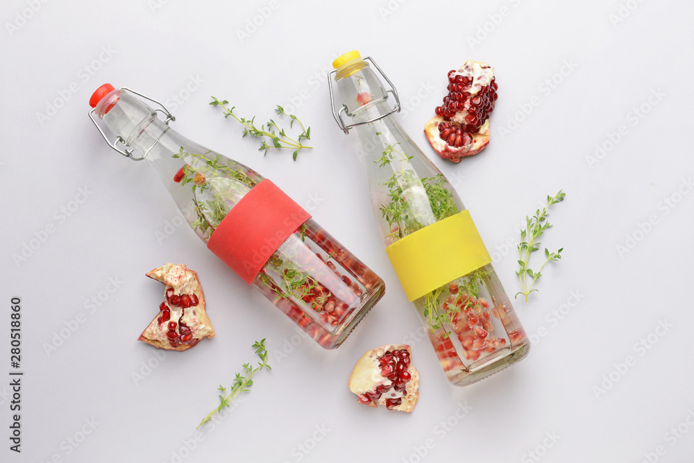 Bottles of infused water and pomegranate on light background