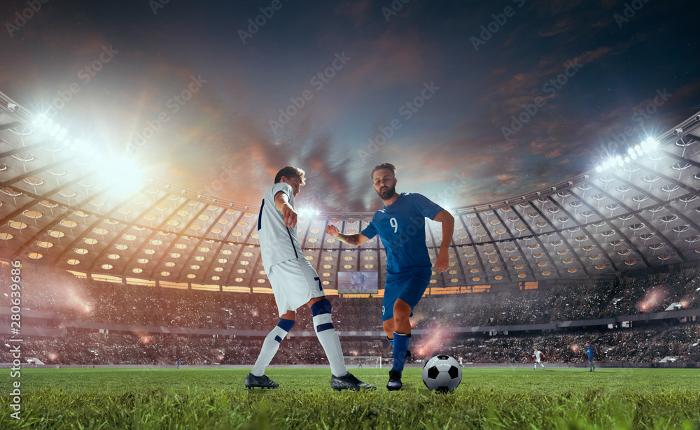 Soccer players in action on professional stadium on sunset.