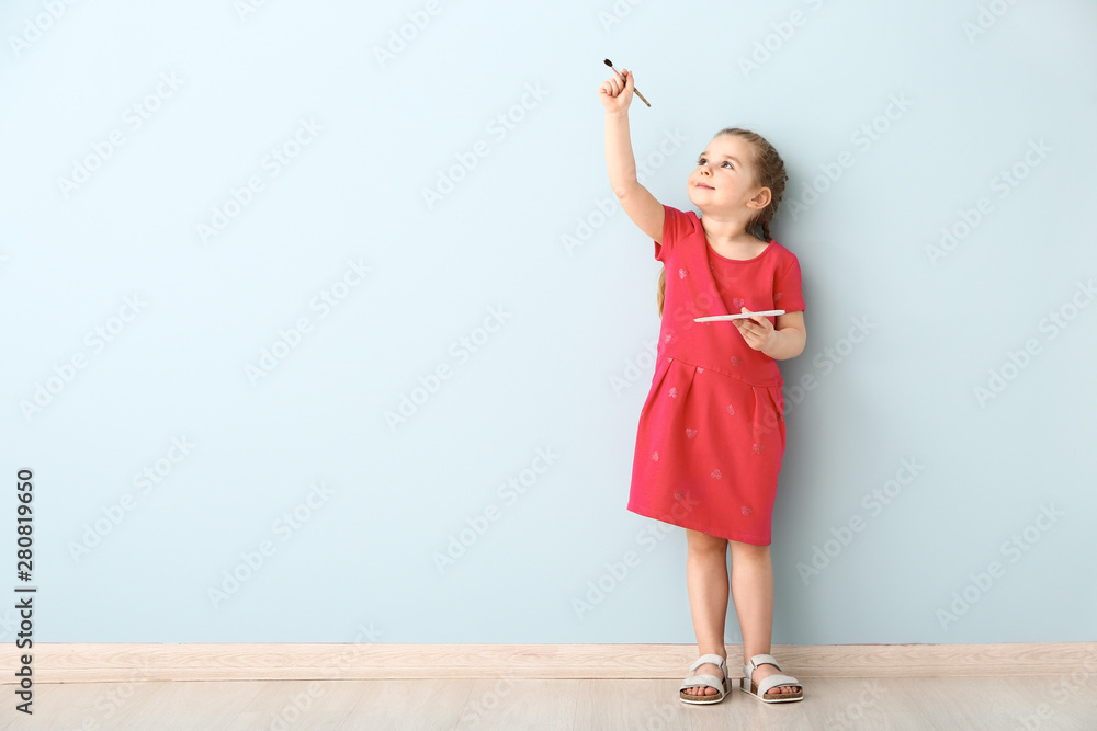 Little girl with brush and palette near light wall