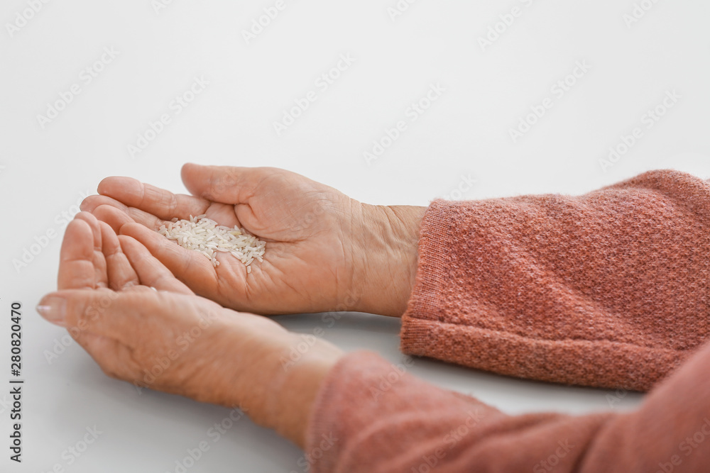 Hands of elderly woman with rice on white background. Concept of poverty