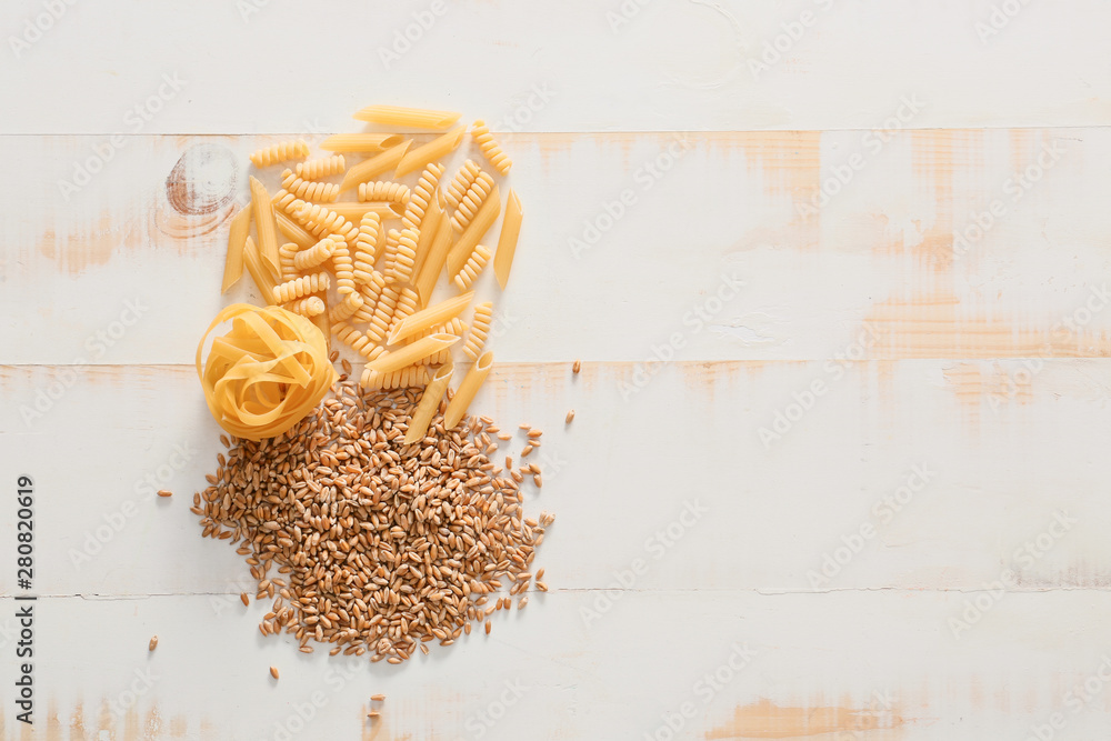 Wheat grains with dry pasta on white wooden background