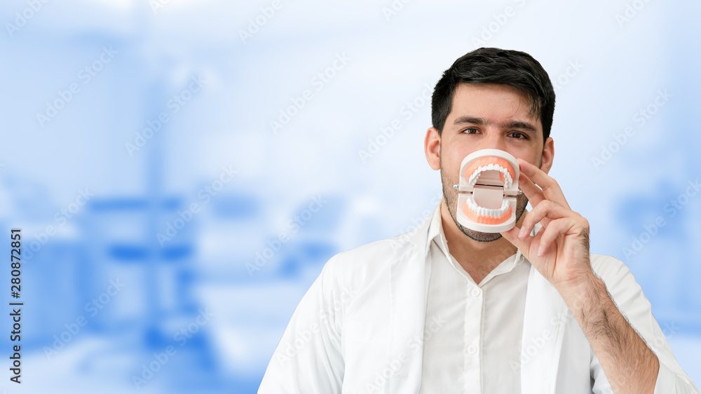 Young male dentist showing toothbrush and denture in dental clinic. Selective focus at the toothbrus