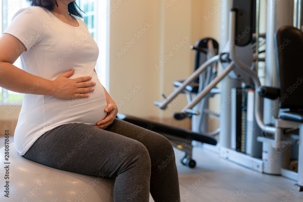 Active pregnant woman exercise in fitness center at yoga room. The young expecting mother holding ba