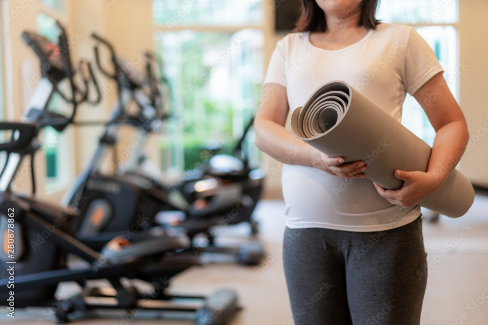 Active pregnant woman exercise in fitness center at yoga room. The young expecting mother holding ba