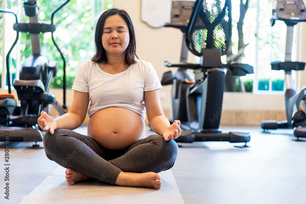 Active pregnant woman exercise in fitness center at yoga room. The young expecting mother holding ba