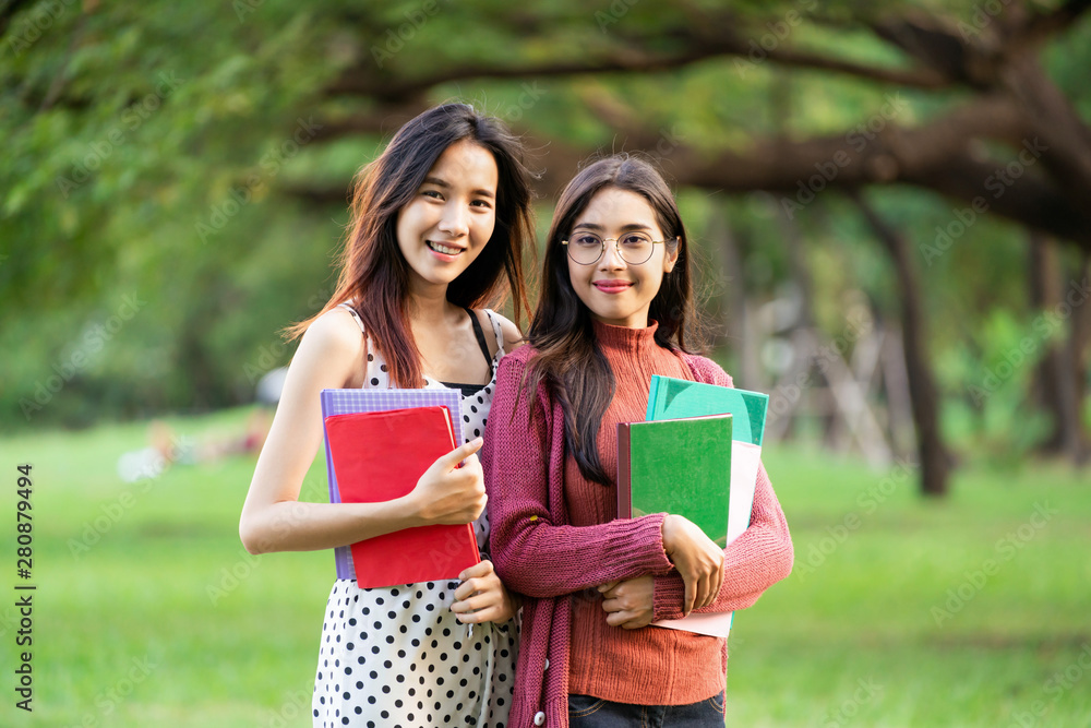 年轻的女学生朋友站在大学公园里手里拿着书。教育总结