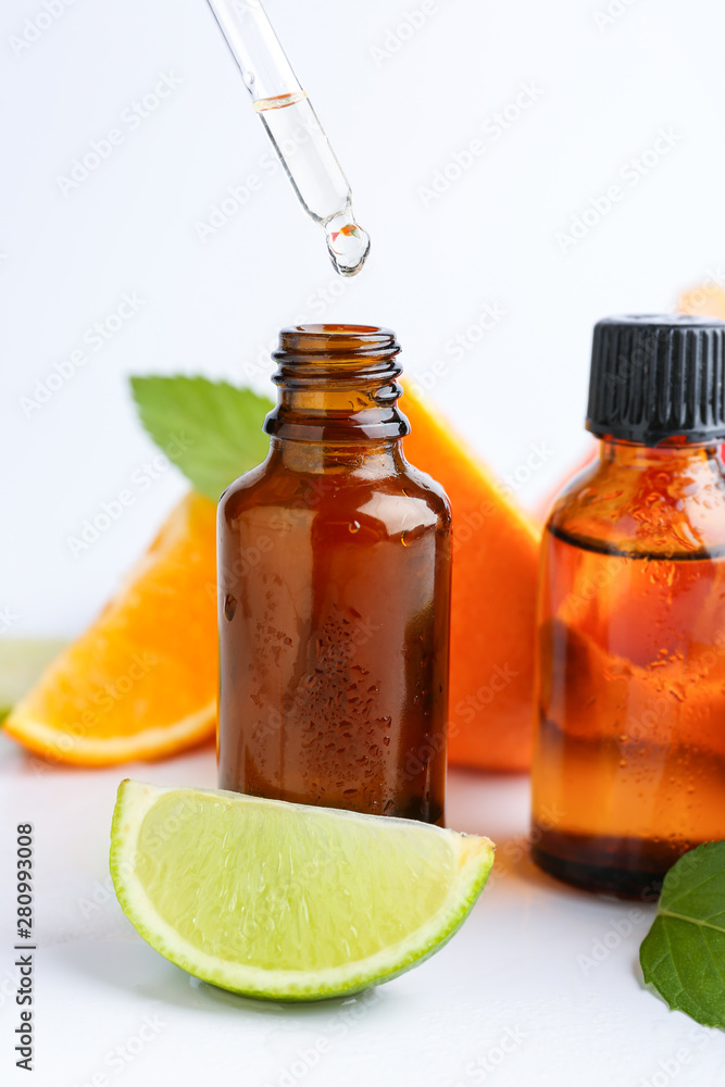 Citrus essential oil dripping from pipette into bottle on white background