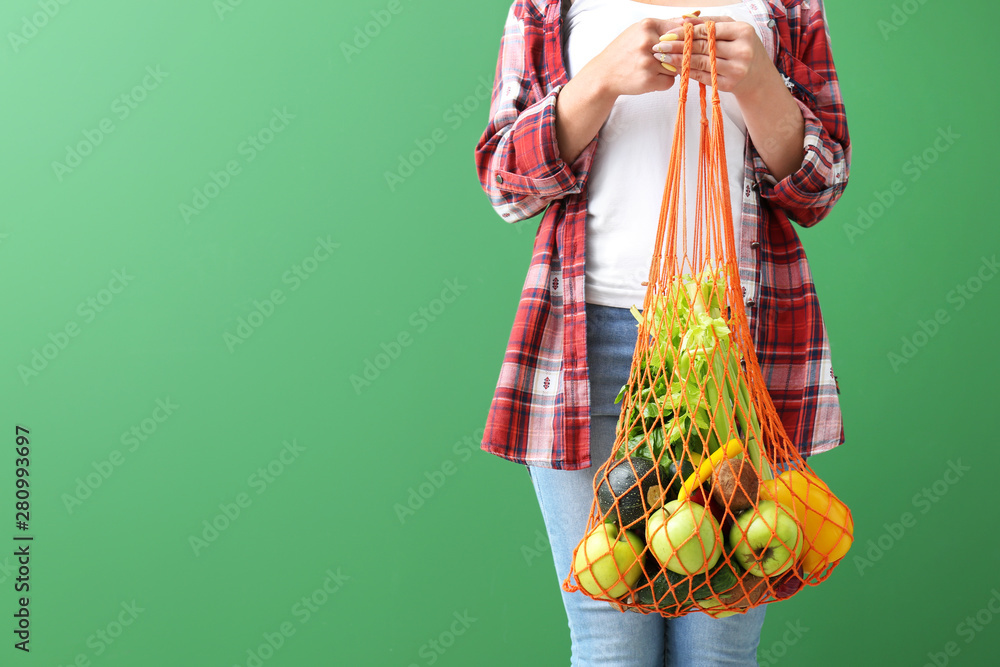 Woman holding mesh eco bag with products on color background