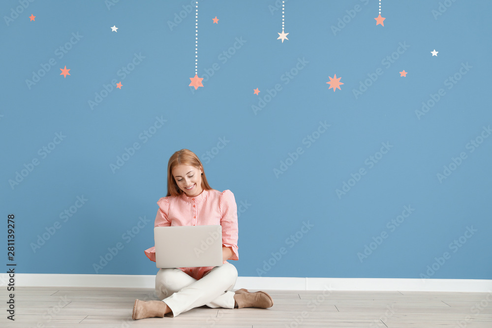 Young female blogger with laptop sitting near color wall