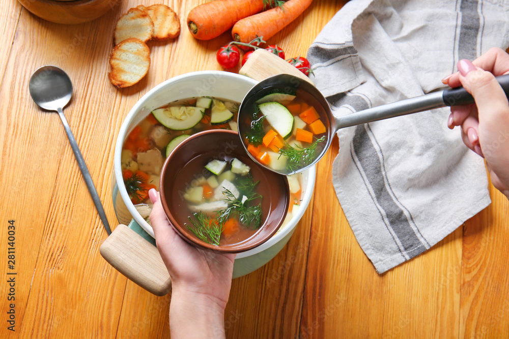 Woman pouring tasty soup from pot into bowl at table