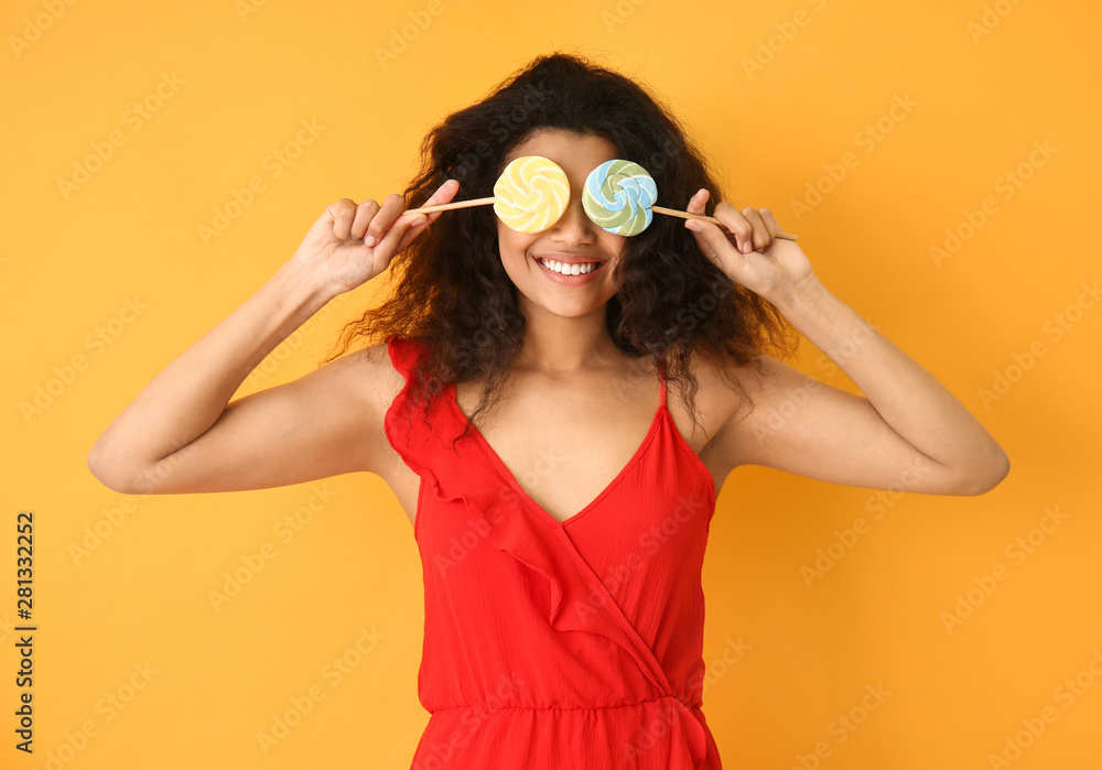 Portrait of happy African-American woman with lollipops on color background