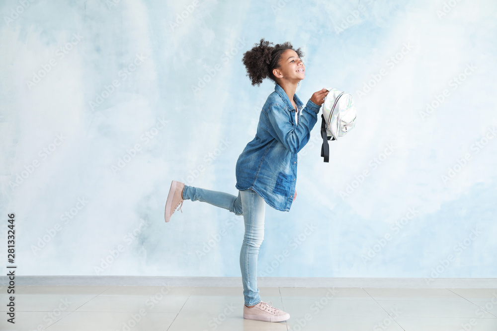 Running African-American girl in jeans clothes and with backpack near color wall