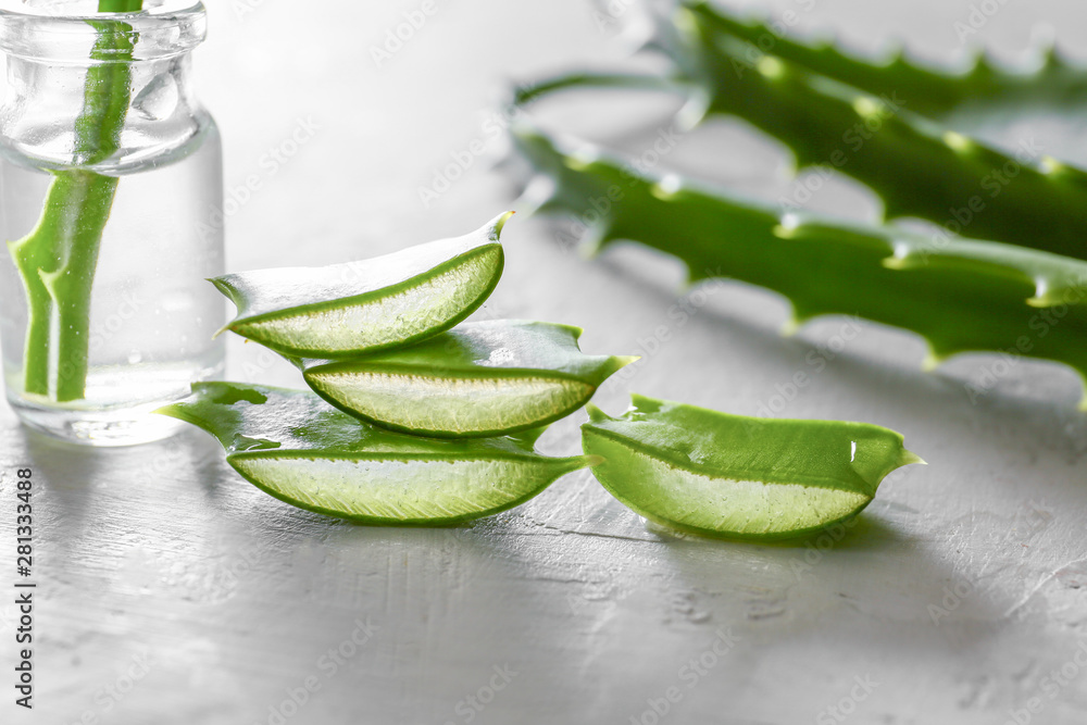 Slices of fresh aloe with essential oil on light background