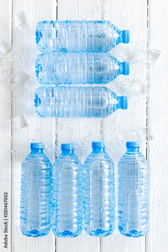 empty plastic bottles for pure water with ice cubes on white wooden background top view