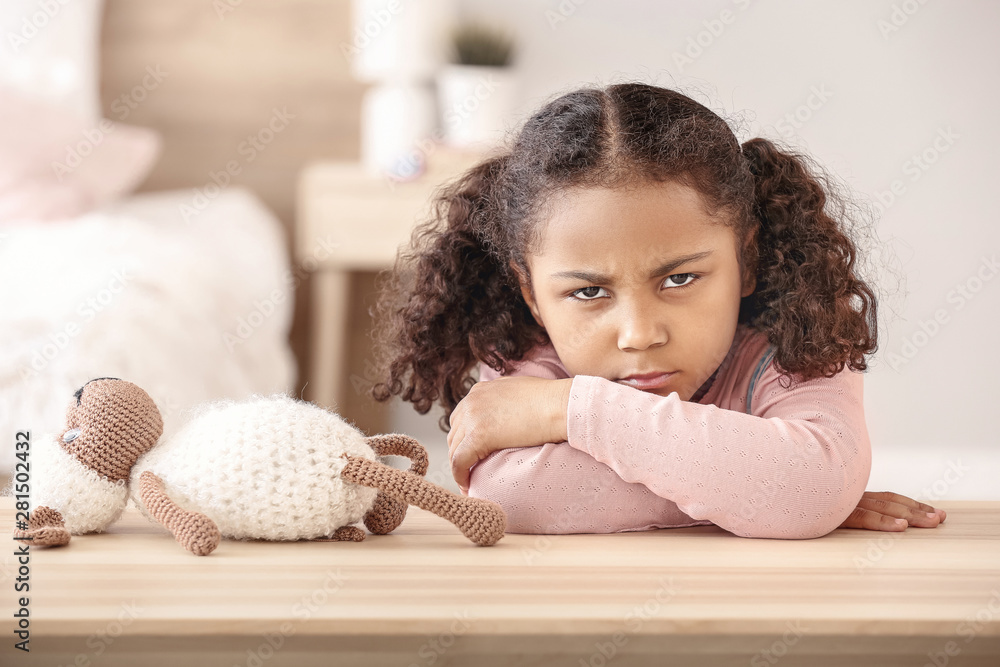 Sad little African-American girl sitting at table