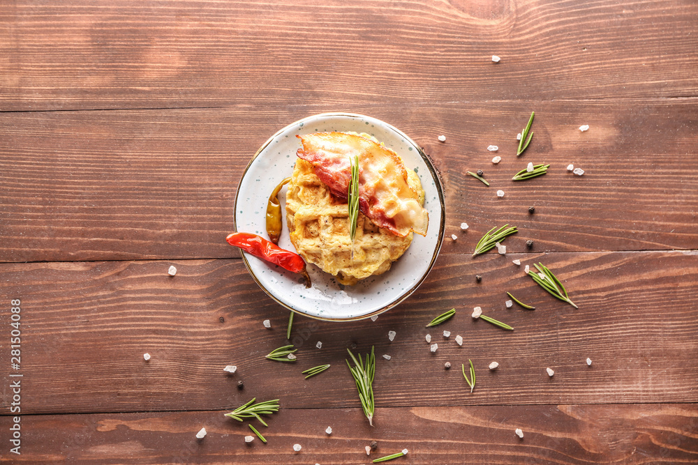 Plate with tasty waffles and fried bacon on wooden background