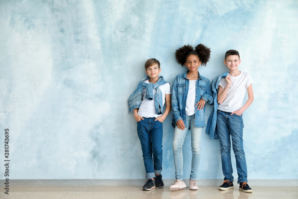 Stylish children in jeans clothes near color wall