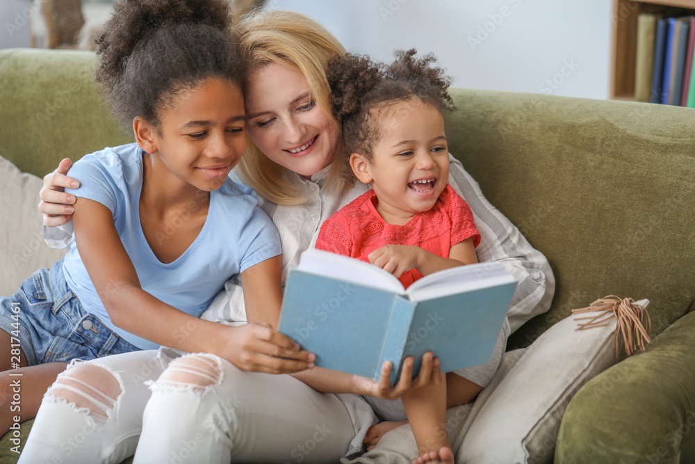 Happy woman with her African-American daughters reading book at home