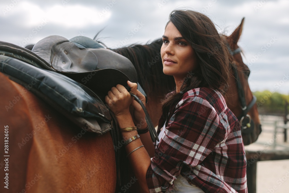 Woman fixing a saddle on her horse