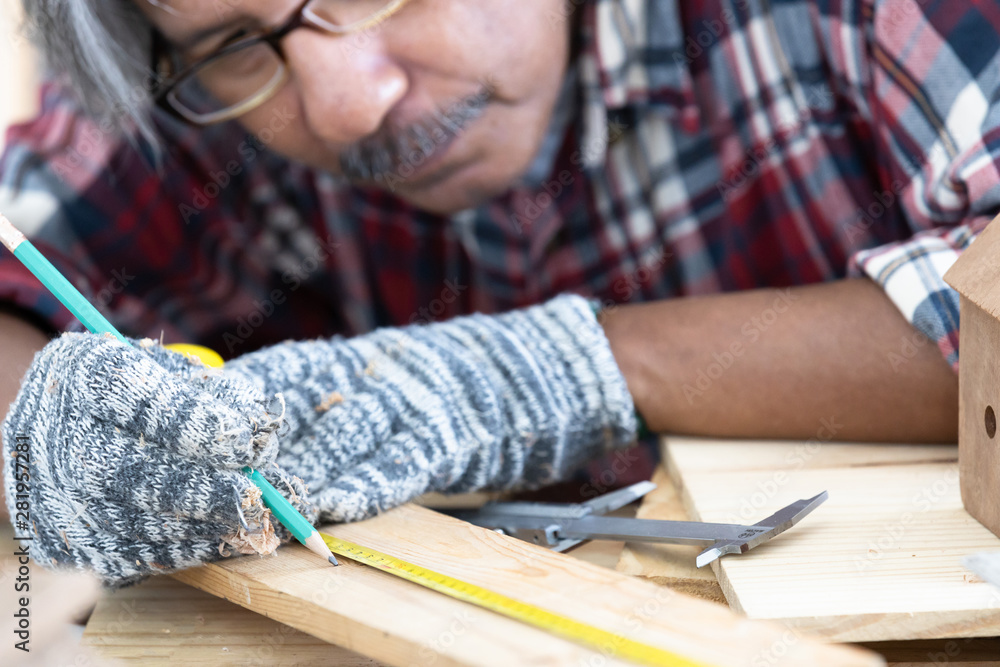 Asian man carpenter working on woodworking table in home carpentry shop, Old asian man works in home